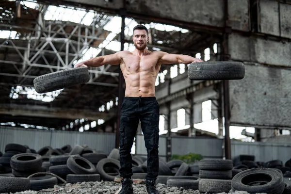 Muscular man lifts tire in his hands.