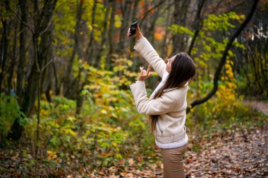 Genç bir kadın sonbahar ormanında selfie çekiyor.