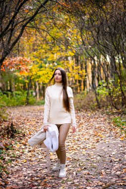 Beyaz kazaklı ve beyaz çantalı güzel bir kadın yürüyor.