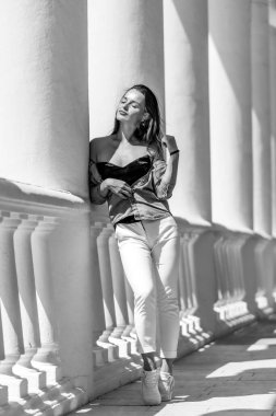 Genç kadın siyah beyaz fotoğrafta kolona yaslanıyor.