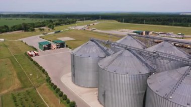 Güncel santraldeki silo konteynerleri. Günümüz tarım fabrikası. Ekinleri depolama ve işleme için. Arkaplanda yeşil tarlalar ve ağaçlar.