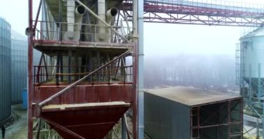 Modern silo fabrikasının tanklarında metal destekler, merdivenler ve borular. Asansörün devasa metal yapısı boyunca yükseliyor. Sisli arkaplan.
