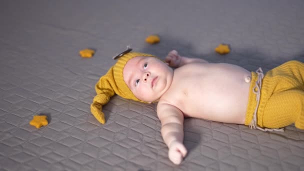 黄色い帽子とベッドの上のズボンで穏やかな小さな子供 赤ちゃんを取り囲む柔らかいおもちゃスター 赤ん坊 — ストック動画