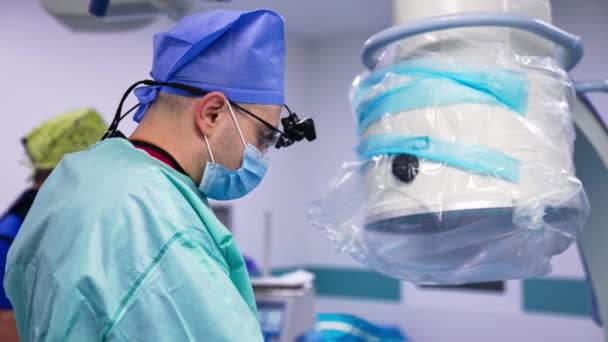 Egy Sebész Kék Egyenruhában Maszkkal Speciális Eszközzel Fején Végzi Műtétet — Stock videók