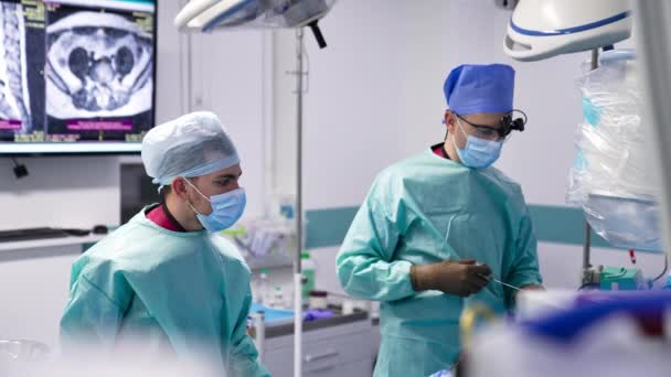 診療室で働く外科チーム 一流の外科医は 彼のアシスタントに 楽器を使った ブラーレッド フォアグラウンド — ストック動画