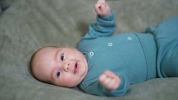 ベッドの赤ん坊は頭が右折した 美しい赤ん坊はカメラとくしゃみを見つめている グレイバックドロップ — ストック動画