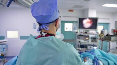 Ameliyat yapan bir cerrah. Erkek doktor hastanın önünde duruyor ve iç organlarını gösteren monitöre bakıyor..