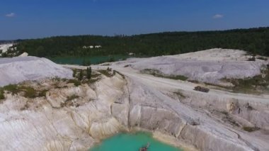 Şimdiki Kaolin madeninde yüklü bir kamyon yol boyunca ilerliyor. Beyaz tepe zemin, mavi su ve temiz gökyüzü. Arkaplanda yeşil ağaçlar.