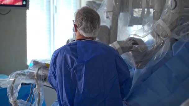 患者の上に立ってモニターを見ている外科医 操作の進捗をコントロールする専門家 カメラに背中を向けて立っている医師 — ストック動画