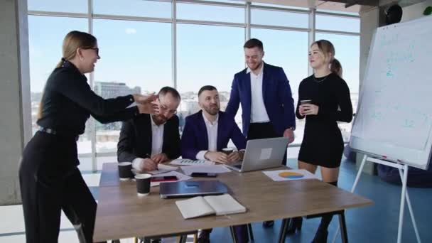 チームワークと同僚間のコラボレーション 男性と女性の同僚は オフィスのテーブルの周りに座って立っています バックグラウンドのシティスケープ — ストック動画