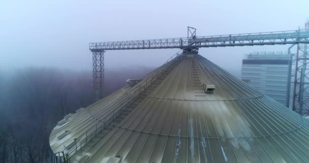 现代电梯的一个巨大的筒仓顶部尘土飞扬 冬季大雾天气时 无人机在银色粮仓上方缓慢飞行 — 图库视频影像