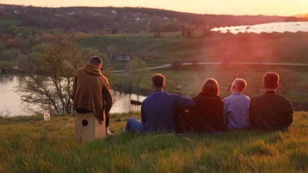 四个年轻男女有很好的野餐时间 观看日落 唱歌和演奏乐器的友爱小组 — 图库视频影像