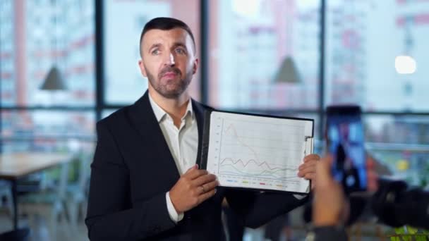 Empresário Segurando Flipchart Com Gráficos Descrevendo Homem Barbudo Falando Emocionalmente — Vídeo de Stock