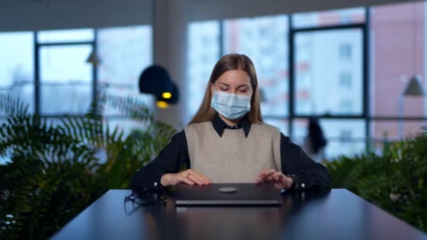 白人女性はオフィスのコンピュータで仕事を終えた 従業員はラップトップを閉め マスクを脱いで幸せに笑顔を浮かべる ブラーレッド バックドロップ — ストック動画