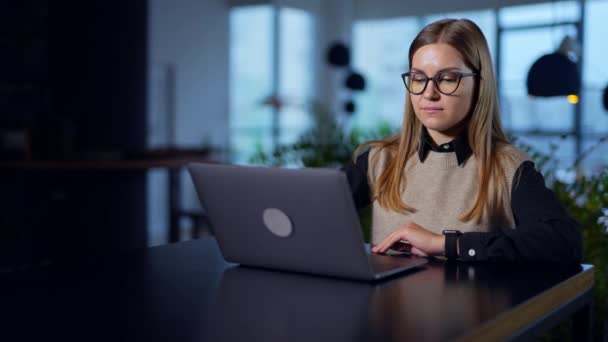 眼鏡のブロンドの女性は 彼女の目の前にテーブルにノートパソコンを開きます オフィスでコンピュータで働く美しい若い女性 バックグラウンド — ストック動画