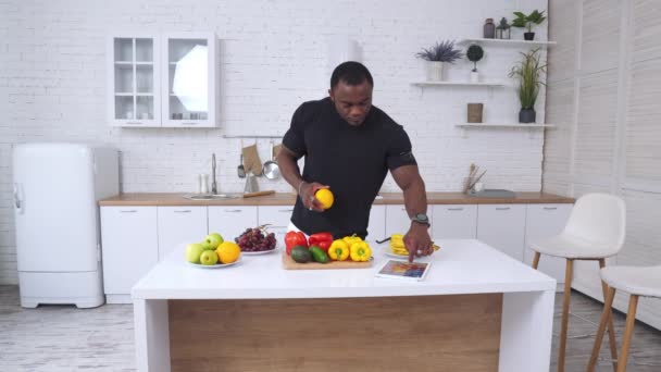 勇敢健康的非洲男人在家里厨房里 英俊的男性选择吃水果 并立即使用Ipad 白色现代厨房背景 — 图库视频影像
