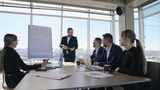 チーム前での感情的なスピーチ テーブルに座り チャートを提示する男を聞いている同僚 同僚のためのオフィスでのビジネスミーティング — ストック動画