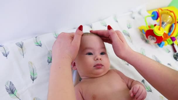 医生的手检查婴儿的头 轻柔而小心地触摸他 可爱的婴儿正在专心地看儿科医生 靠近点 — 图库视频影像
