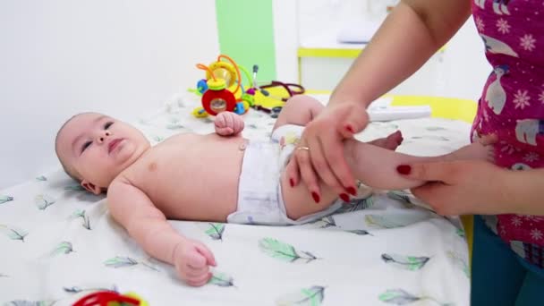 男婴正在接受外科医生的检查 女医生检查婴儿的腿和膝盖 背景中的玩具 — 图库视频影像