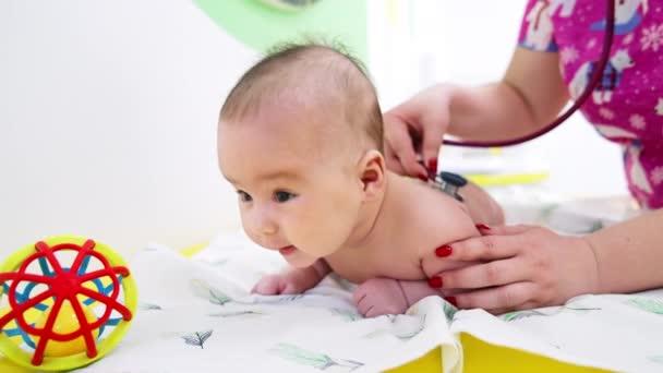 可爱的婴儿赤身裸体躺在肚子上 抬起头来 儿科医生把听诊器放在小孩的背上 靠近点 — 图库视频影像