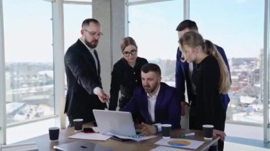 Ofis atmosferinde işbirliği ve takım çalışması. İnsanlar dizüstü bilgisayara bakarak fikir ileri sürüp tartışıyorlar. Arka planda şehir manzarası.