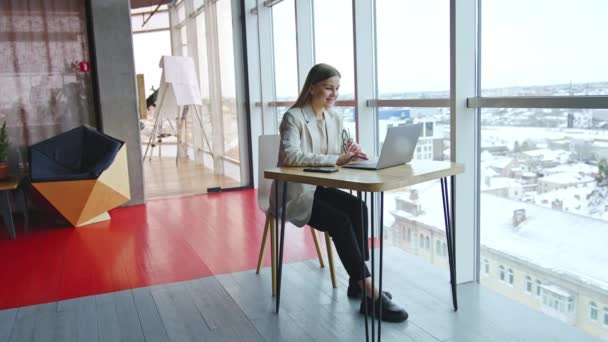 明るい広々としたオフィスの職場で働く若い女性 デスクに座ってラップトップで働くビジネスレディ バックドロップのシティスケープ — ストック動画