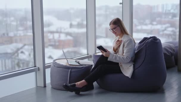 年轻的女员工坐在豆袋扶手椅上 看着她的手机 现代办公室的工作空间不错 — 图库视频影像