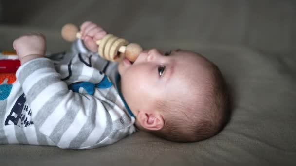 Küçük Bebek Ağzına Tahta Bir Oyuncak Aldı Çizgili Kostümlü Yatakta — Stok video