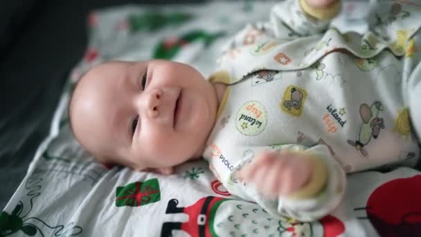 活泼健康的男婴躺在床上 张开嘴 甜甜地笑着 精力充沛的孩子高兴地挥动着手和腿 靠近点 — 图库视频影像
