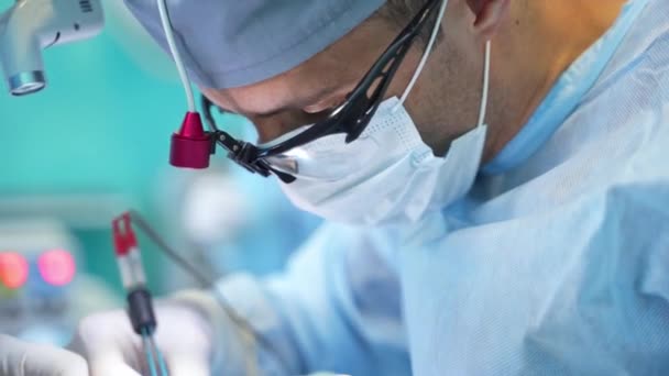 衣装とデバイスのメガネの外科医は 正確な作業を行います 手術中に医師の肖像画を閉じる ブラーレッド バックドロップ — ストック動画