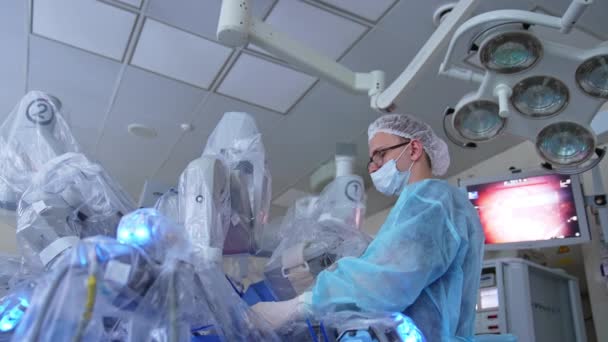 ロボット機器の作業を監視するマスクの外科医 近代的な演劇の先端技術装置 ローアングルビュー — ストック動画