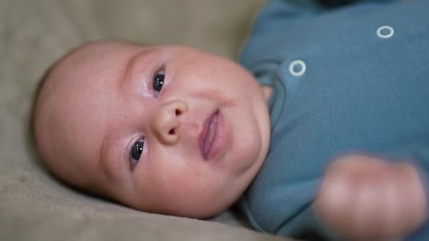 ベッドの上に横たわり カメラを見ている白人少年 愛らしい赤ちゃんの顔は 舌を小さくする クローズアップ — ストック動画