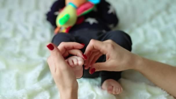 母亲把婴儿的小脚抱在怀里 孩子躺在床上 手里拿着玩具 神智不清 白色背景 — 图库视频影像