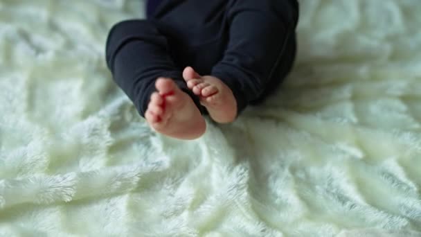 一个婴儿的小脚躺在床上 穿着深色裤子的小孩抛掷小腿 靠近点白色背景 — 图库视频影像