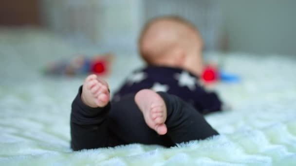 白い平原の上の愛らしい幼児は カメラの足に横たわっています 小さな足を投げている赤ん坊の少年 クローズアップ ブラーレッド バックドロップ — ストック動画