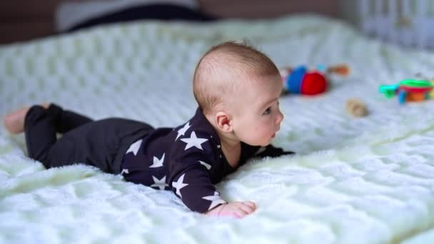 小さな幼児はベッドに横たわるように頭を抱えようとする 優しい子供は自分の前を注意深く見つめている サイドビュー — ストック動画