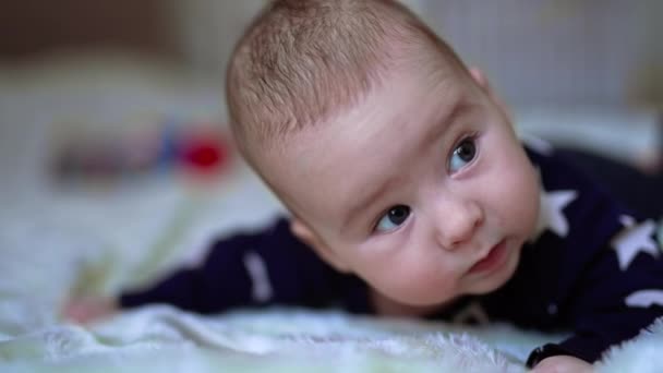 可爱的白人男婴抬起头 睁大了眼睛 可爱的孩子在床上 靠近点模糊的背景 — 图库视频影像