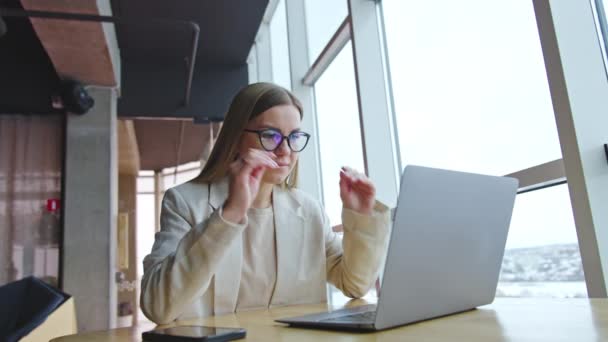ノートパソコンの前に座って注意深く観察する女性社員 女の子はメガネを外して それらを下に置きます 女性は元気な笑顔で — ストック動画