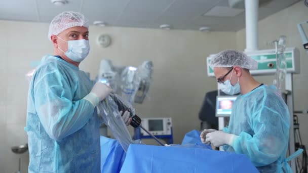 プロの外科医が手術を行っています 1人の外科医は技術装置を持ち もう1人はスカルペルを使用しています ブラーレッド バックドロップ — ストック動画