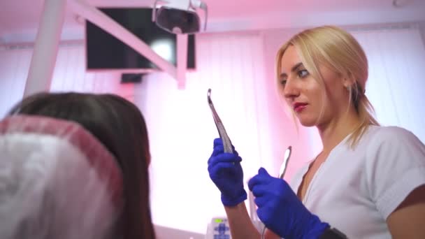 金属工具を持っているブロンドの女性歯科医 医師は患者に楽器を適用し 満足のいく笑顔を提供する クローズアップ — ストック動画
