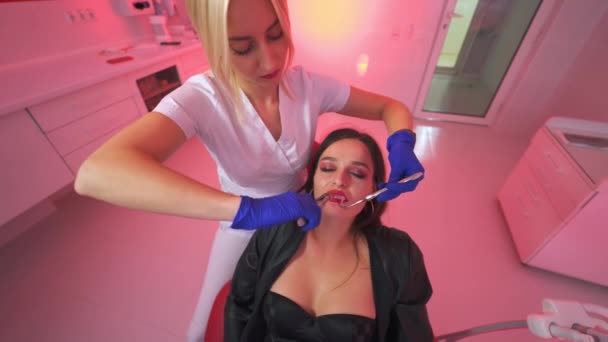 金发女牙医拔出吸血鬼的牙齿 黑头发的女人穿着黑色衣服 是牙医的病人 高角度视图 — 图库视频影像