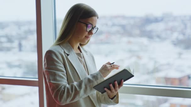 Μια Νεαρή Γυναίκα Κρατάει Σημειώσεις Στο Βιβλίο Της Στο Παράθυρο — Αρχείο Βίντεο