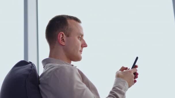 若者は椅子に座り 目の前に電話をかけている 白い背景にある男性の側面図 — ストック動画
