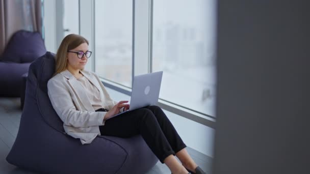 ノートパソコンで働く女性起業家 レディースは大きなパノラマウィンドウの近くに快適な椅子に座っています — ストック動画