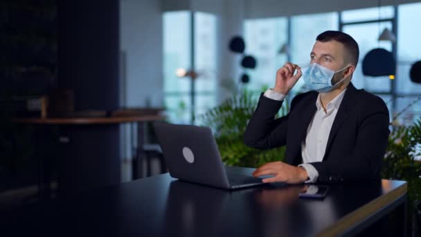 男性起業家はマスクを外してノートパソコンを閉じた ひげ付きの男は仕事を終え それに満足した バックドロップのブレイクオフィス — ストック動画