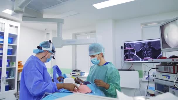 外科医は患者の鼻にカメラを搭載した装置を置きます チーフドクターは彼の前にスクリーンの操作プロセスを調べる — ストック動画