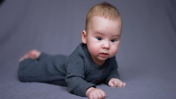 Słodki Chłopczyk Szarym Ubraniu Leży Brzuchu Zdrowe Dziecko Rozgląda Się — Wideo stockowe