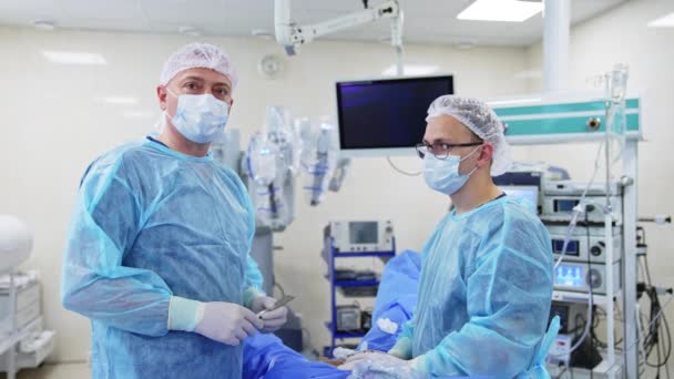 外科手術の準備をする外科医 金属製の道具を持っている2人の医療専門家がカメラに話しかけます バックドロップのロボット機器 — ストック動画