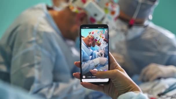 Ženská Ruka Drží Telefon Pořizuje Video Operujících Chirurgů Zavřít Backdrop — Stock video