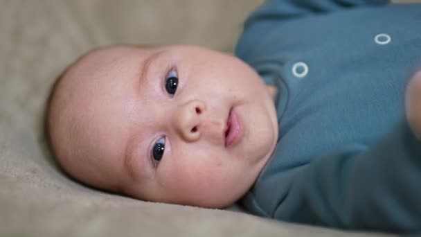 背中に横たわっている健康な白人子供 カメラをじっと見つめている美しい平和な赤ちゃんの顔の肖像画 — ストック動画